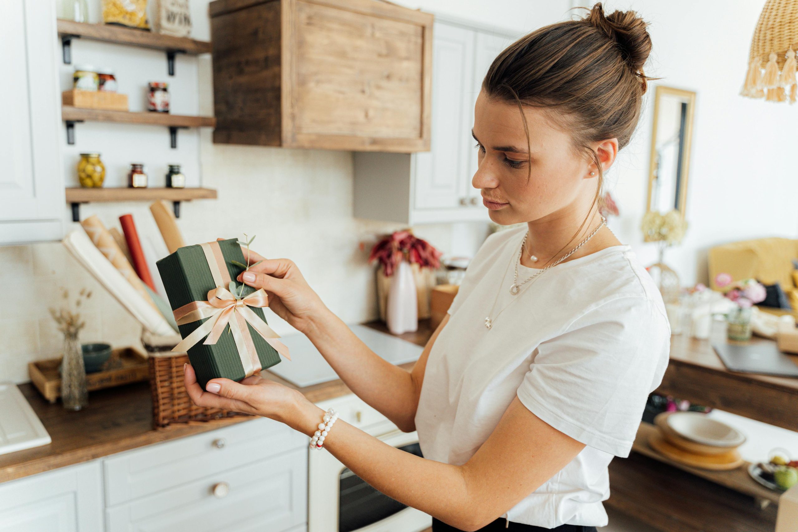 Young woman with gift box, standing in a warm, stylish kitchen.