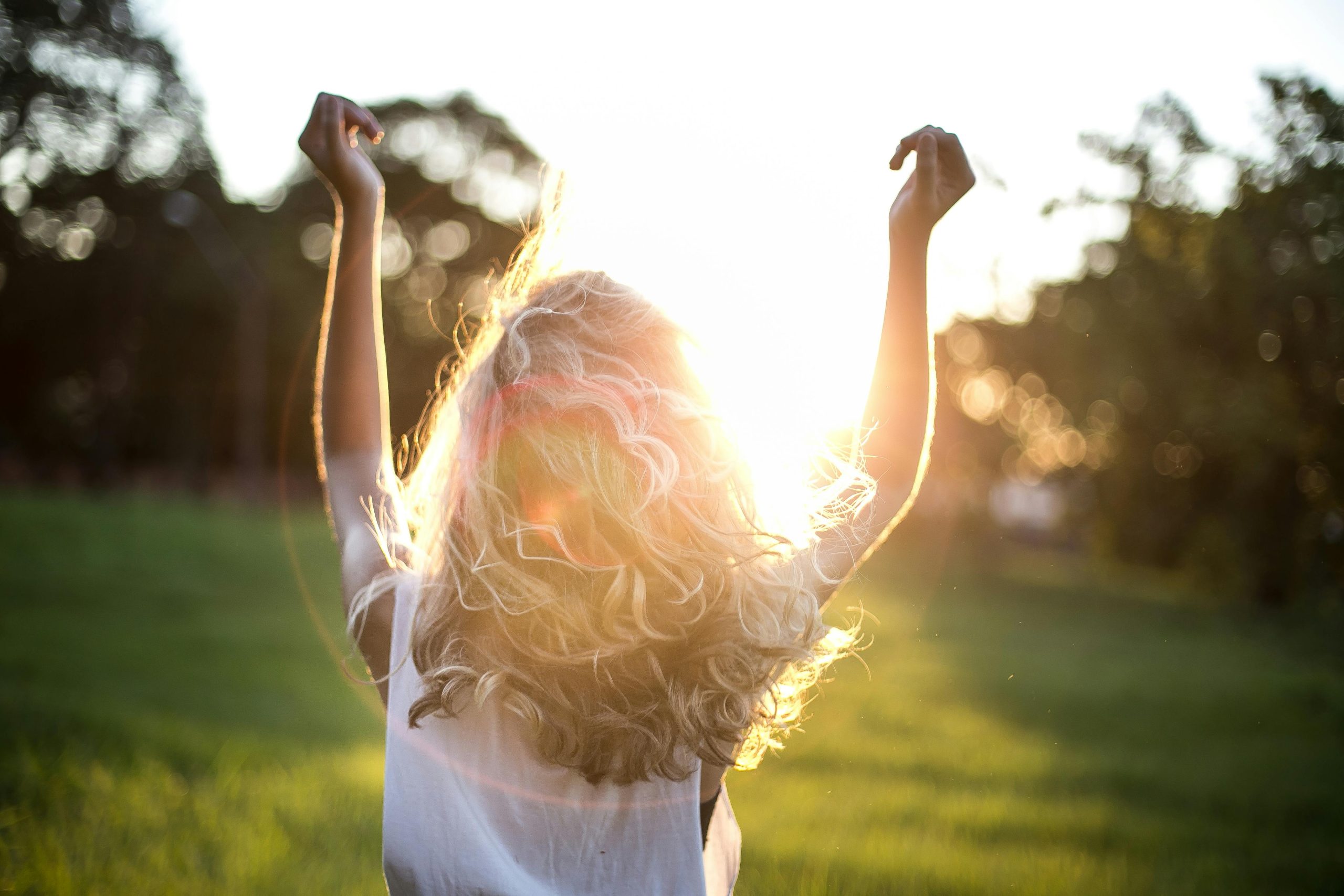 A woman with outstretched arms celebrates the sunset in a grassy field, capturing the essence of freedom and joy.